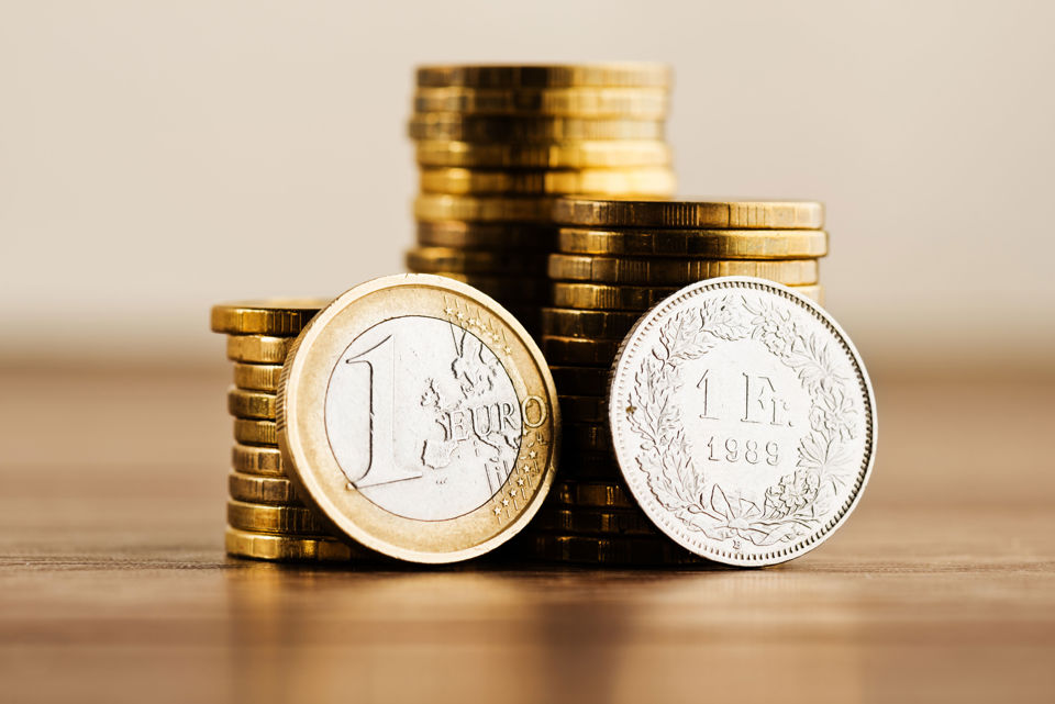 Münzstapel, an dem nebeneinander eine 1-Euro-Münze und eine 1-Franken-Münze lehnen