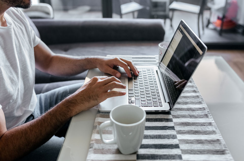 Frau trinkt am Bürotisch neben Laptop einen Kaffee