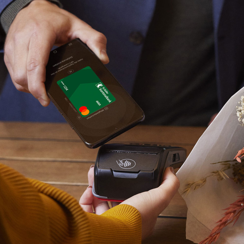 Smartphone mit SGKB Debit Mastercard in Samsung Pay wird fürs Bezahlen an ein Zahlterminal gehalten

