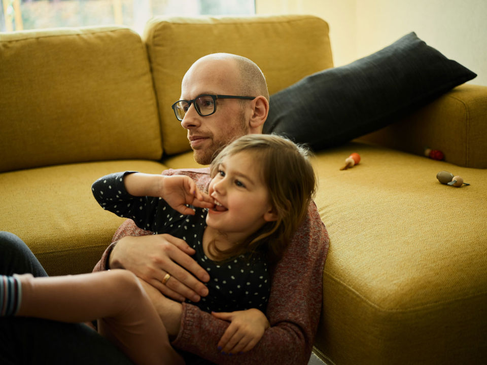 St.Galler Finanzberatung - Ein Vater und seine kleine Tochter sitzen vor der Couch und schauen etwas an
