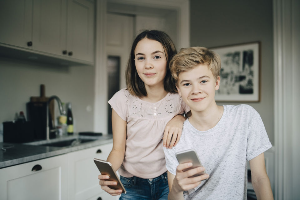Jugendbudget - Zwei Kinder schauen lachend in die Kamera und halten ihre Smartphones in Händen