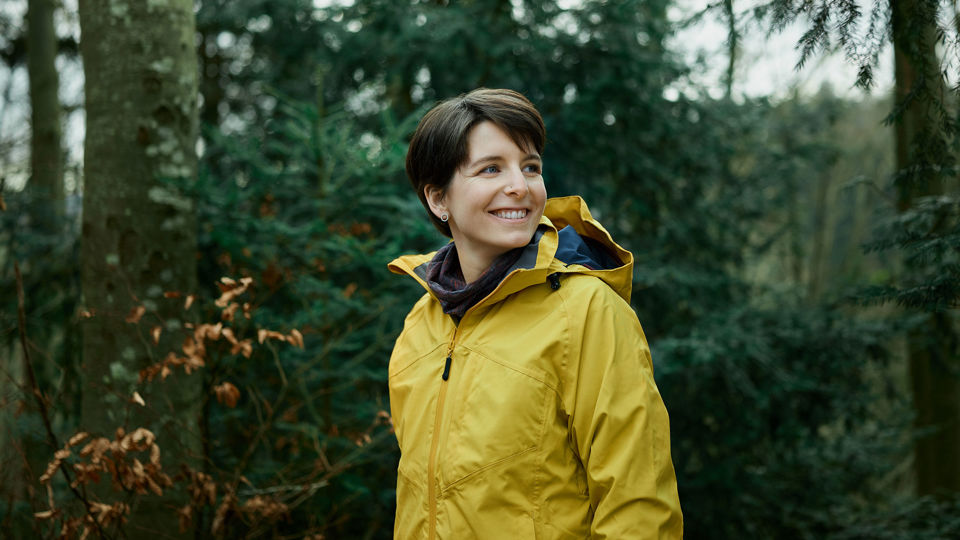 Eine glückliche Frau in gelber Regenjacke beim Waldspaziergang