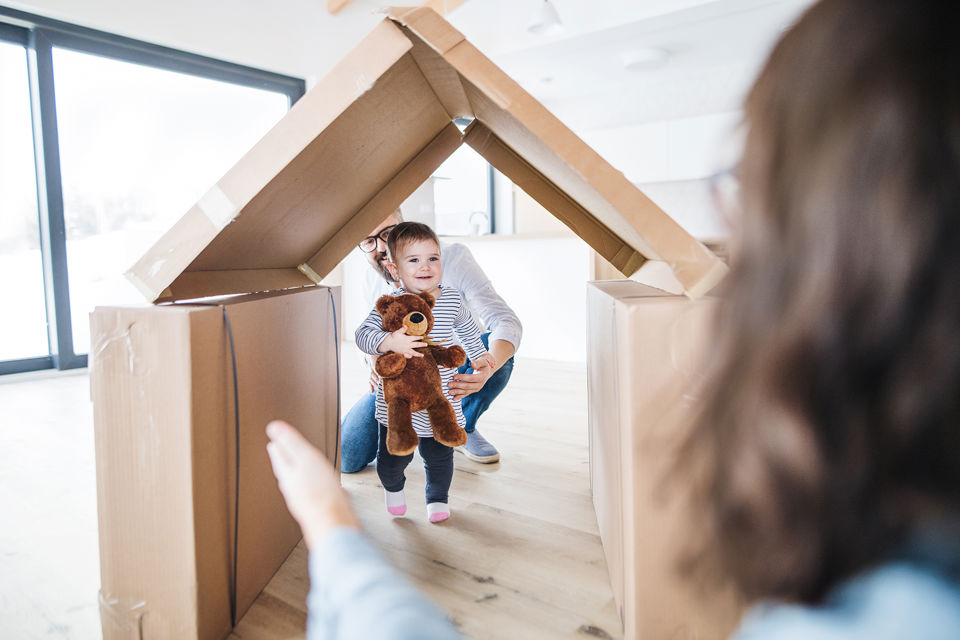 Ein Kleinkind spielt mit den Eltern im Eigenheim in einem aus Kartons gebauten Haus