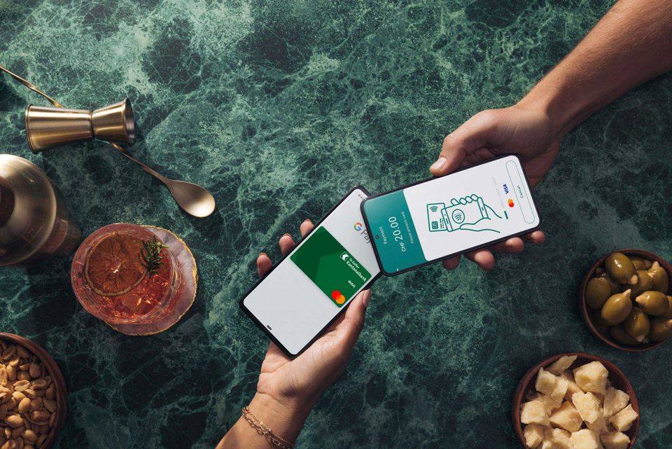 Zwei Personen halten in einer Bar Ihre Smartphones aneinander und teilen die Rechnung untereinander mit den Bezahllösungen Worldline Tap on Mobile und Google Pay