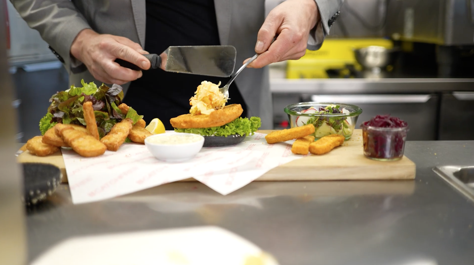 Mann bereitet pflanzliche Fischknusperli auf einem Teller zu