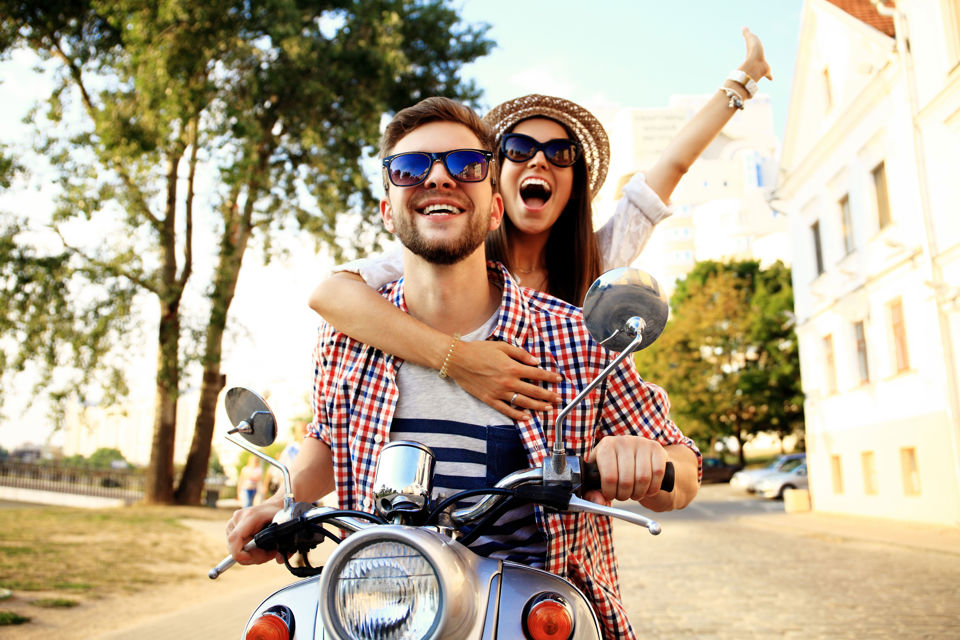 Ferientipps - ein junges Paar sitzt in Ferienkleidung auf einem Roller