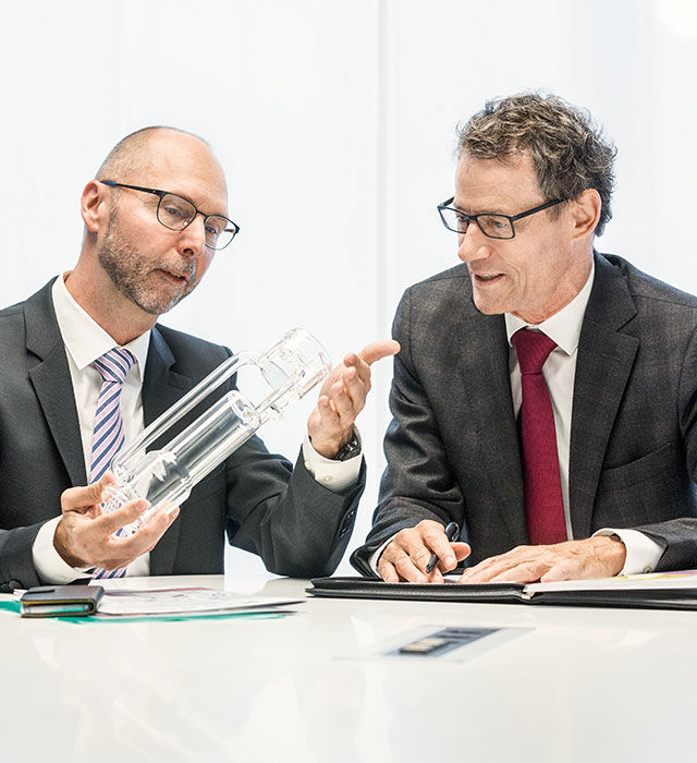 Zwei Männer in einer Besprechung schauen sich einen gläsernen Gegenstand an