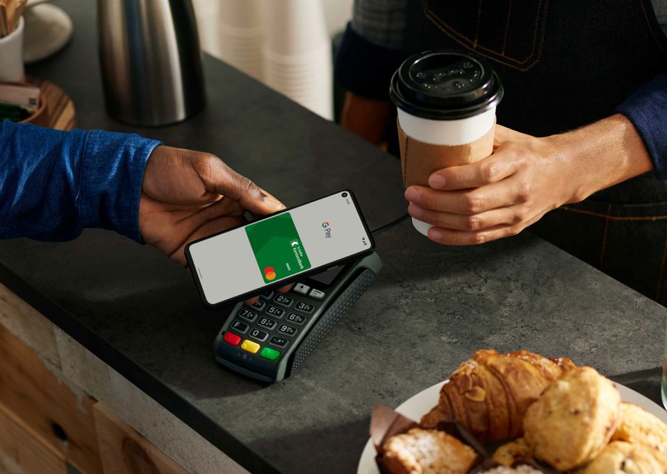 Eine Person bezahlt an einem Zahlterminal per Smartphone und der SGKB Debit Mastercard in Google Pay 