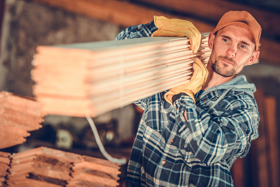 Arbeiter in einem Sägewerk trägt einen Stapel Holzbretter auf den Schultern