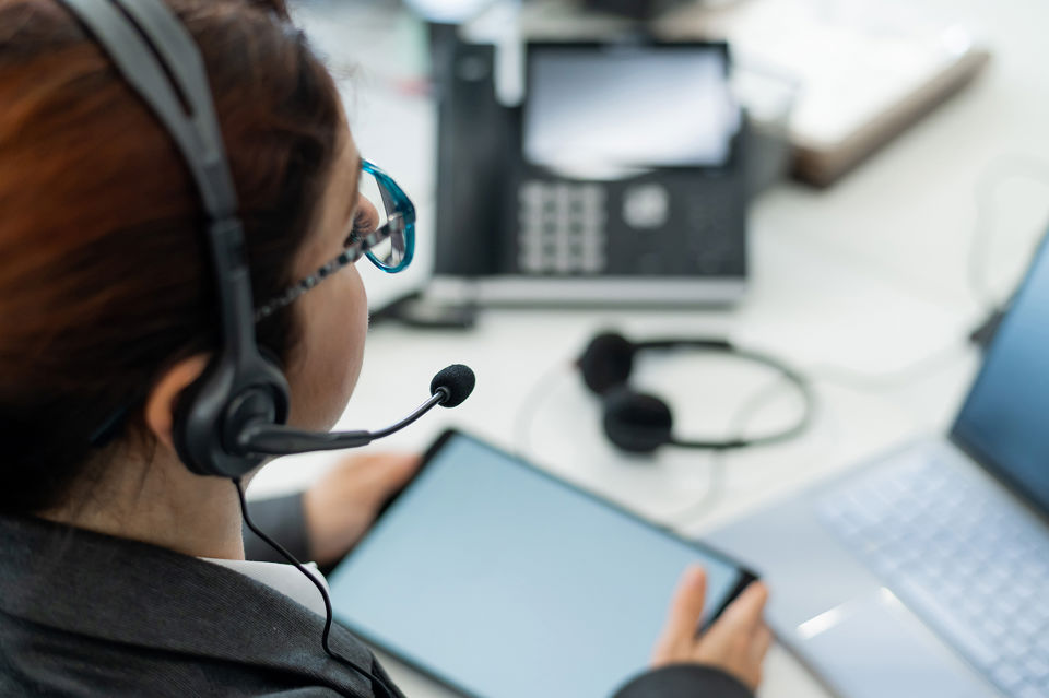 Eine Frau sitzt vor einem Laptop und nimmt per Headset Anrufe entgegen