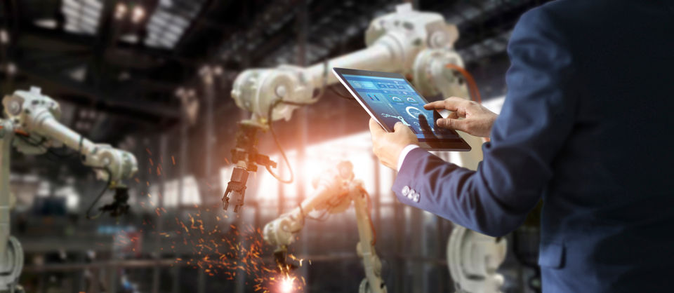 Person mit Tablet steuert Roboter in einer Fabrik