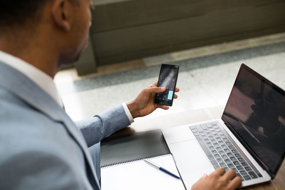 Ein Mann arbeitet am Laptop und verwendet den Taschenrechner auf seinem Smartphone
